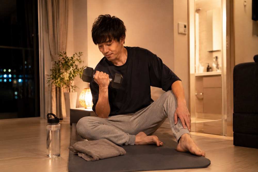 夜の部屋でお風呂の前にダンベルで軽い筋トレをする男性