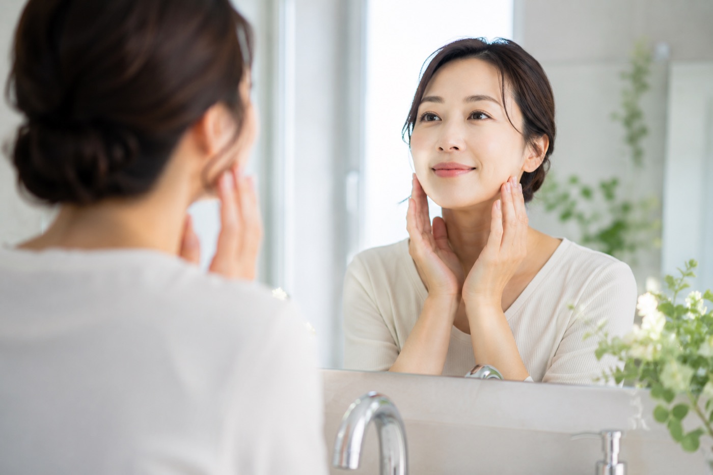 鏡の前でフェイスラインにやさしく手を添える女性